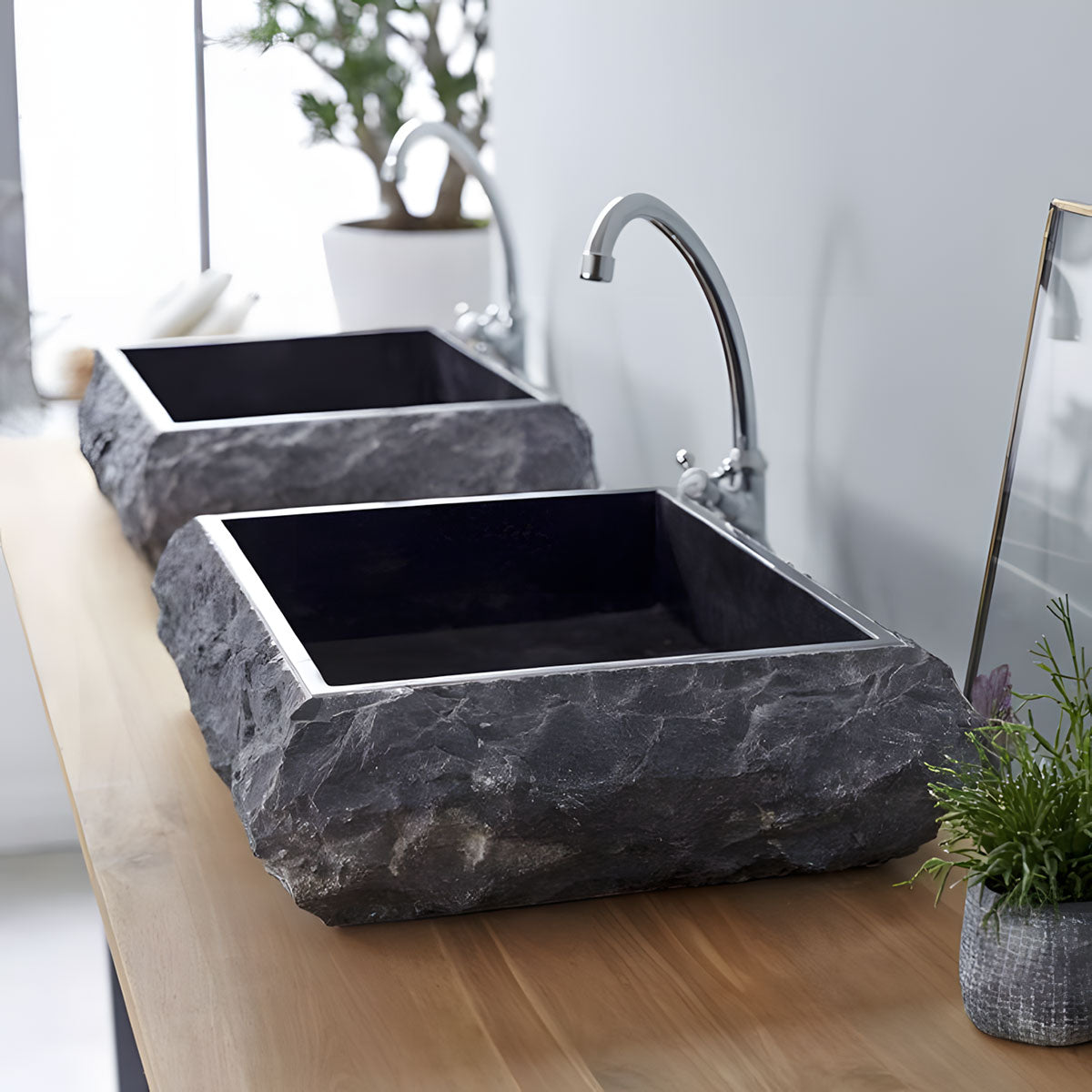 Dark black travertine vessel sink with hand chiseled rough uneven edge rectangular natural stone basin displayed on wooden bathroom vanity countertop